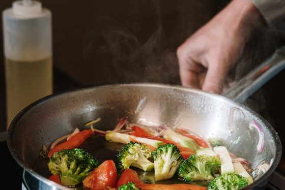 Close-up of sautéing broccoli and bell peppers in a pan on a stove.
